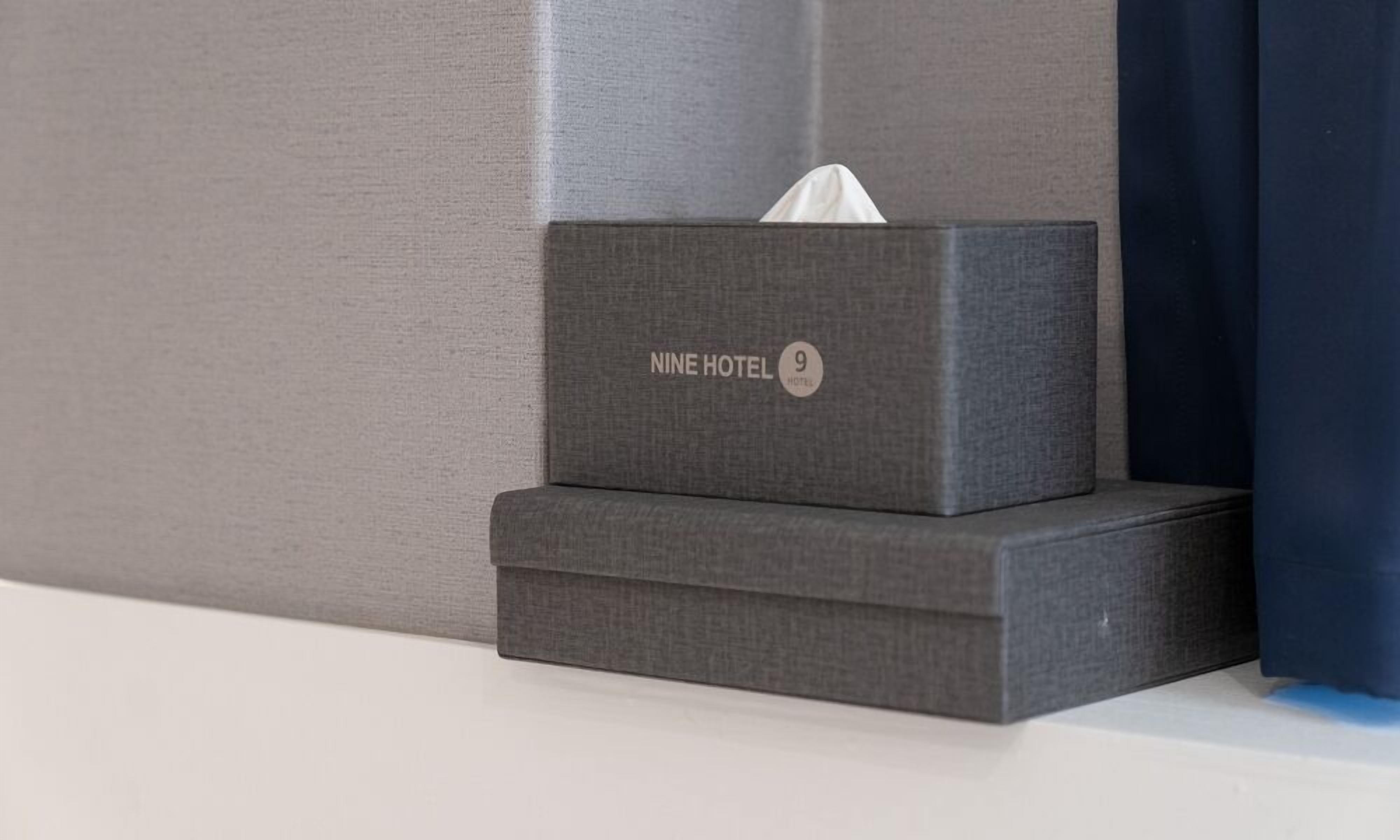 A tissue box with 'NINE HOTEL' branding on a hotel room wall.