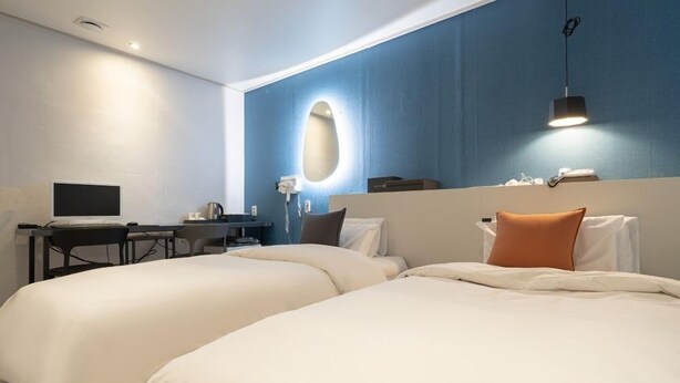 A hotel room with two beds, a desk with a computer, a phone, and a wall-mounted light fixture. - Hotel Nine (Uiwang)