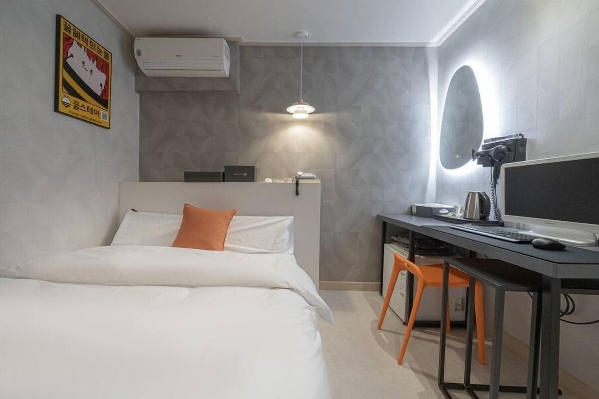 Quarto de hotel com cama, escrivaninha, computador e ar-condicionado fixado na parede.