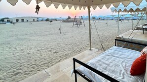 A beachside tent with a bed and a view of the beach and distant buildings. - Osaka Desert Safari Camp (Jaisalmer)