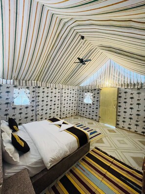 A tent-style room with a bed, patterned curtains, and a ceiling fan. - Osaka Desert Safari Camp (Jaisalmer)