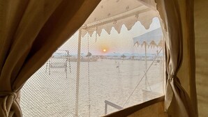 A window with sheer curtains and a view of a building with scaffolding. - Osaka Desert Safari Camp (Jaisalmer)