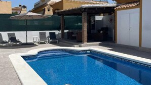Une piscine à l’eau d’un bleu limpide, avec une échelle en métal et des chaises longues.