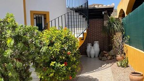 Une cour intérieure avec un escalier menant à un deuxième étage, entourée de plantes en pot et d’un mur de briques.