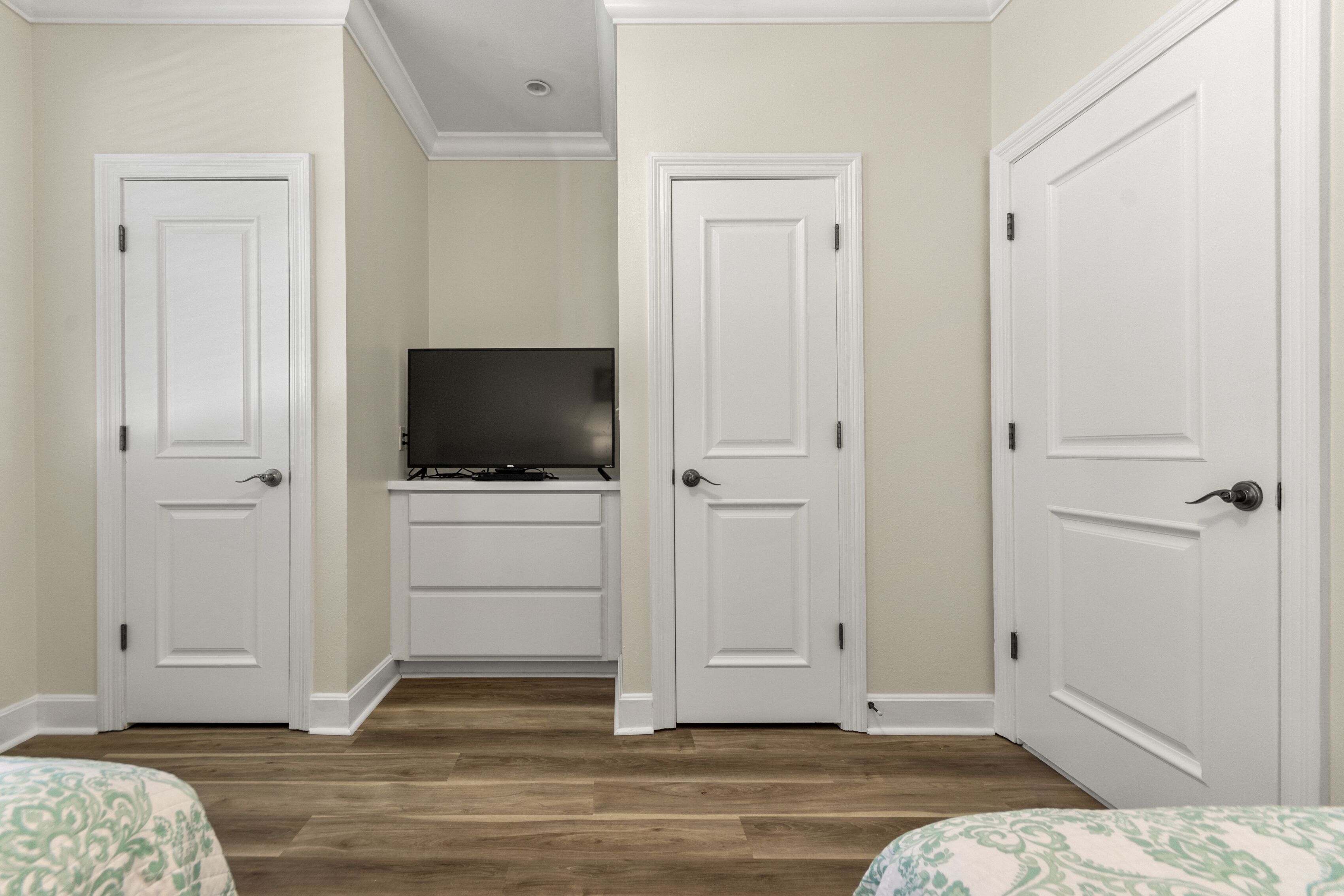 Un dormitorio con dos camas, un televisor sobre un mueble y puertas blancas.