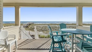 Ein überdachter Außenbereich mit Holzdeck, weißen Geländern und Blick auf Strand und Meer.