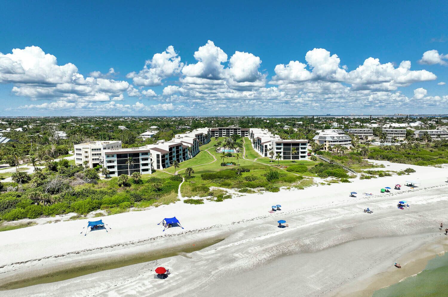 Ein Strandhotel mit mehreren Gebäuden, einem Sandstrand und einem wolkenlosen, blauen Himmel.