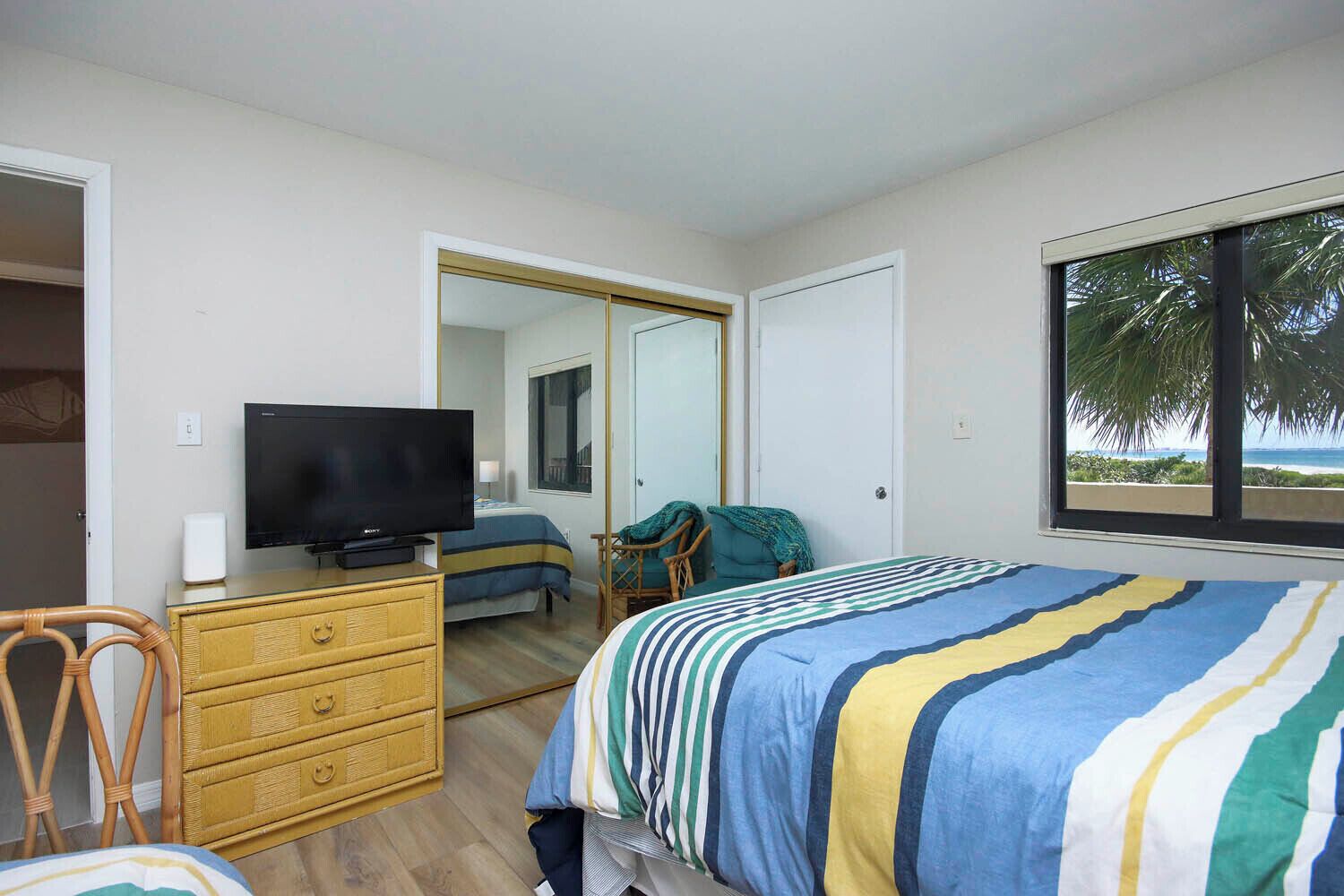 A bedroom with a bed, a television, a dresser, a chair, and a window with a view.