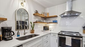 Een moderne keuken met witte kasten, een roestvrijstalen fornuis, een koffiezetapparaat en een spiegel met houten lijst.
