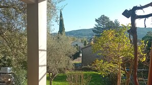 A covered outdoor area with a view of a garden and distant hills.