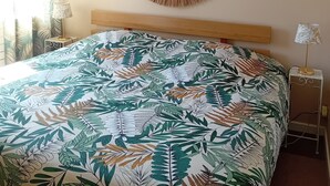 A bedroom with a large bed, a round wall hanging, a nightstand with a lamp, and curtains with a leaf pattern.