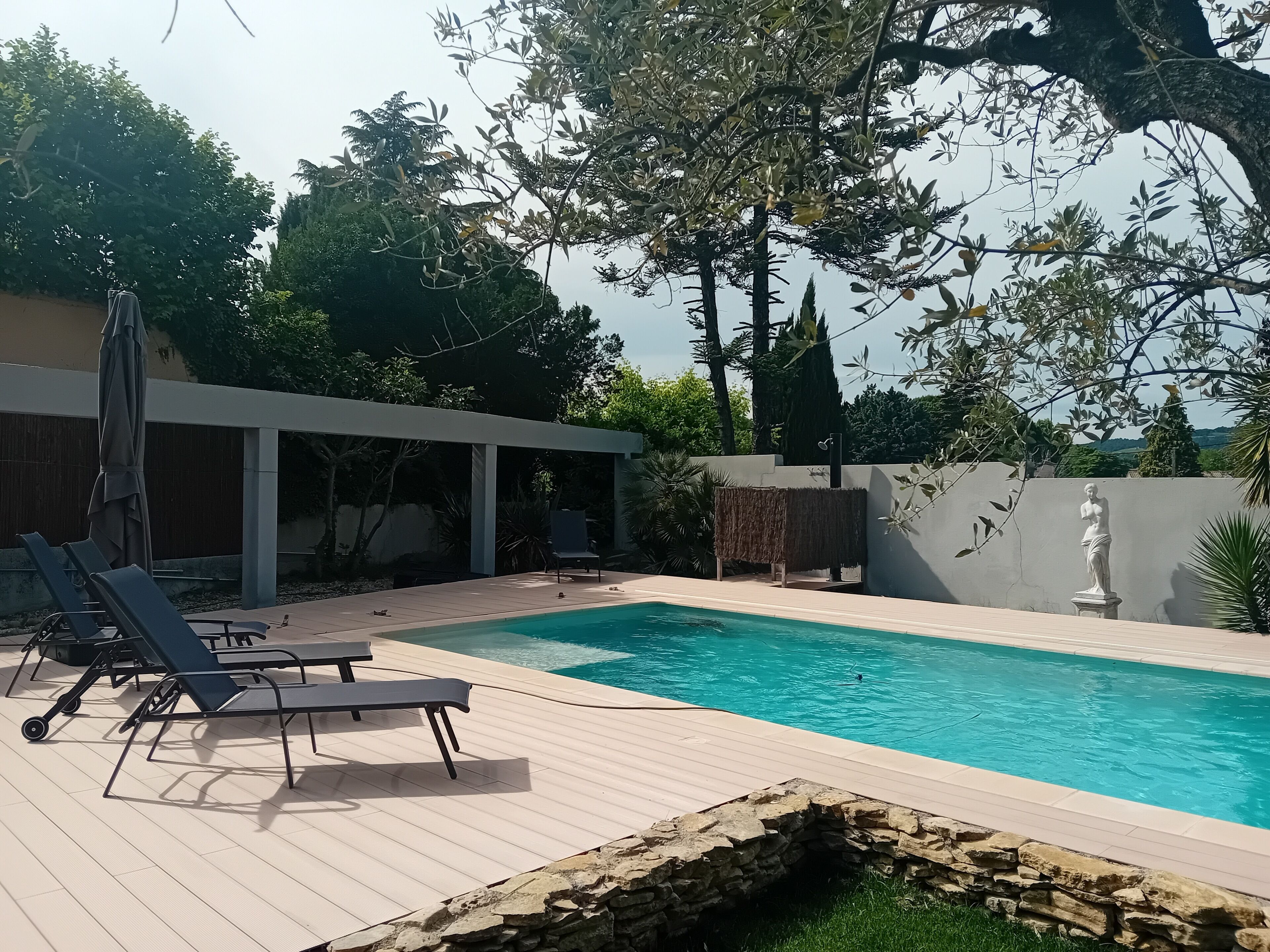 Una piscina con lettini e una statua, immersa nel verde e affiancata da un edificio moderno.