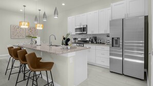 Una cocina moderna con armarios blancos, electrodomésticos de acero inoxidable y una isla central con taburetes de bar.