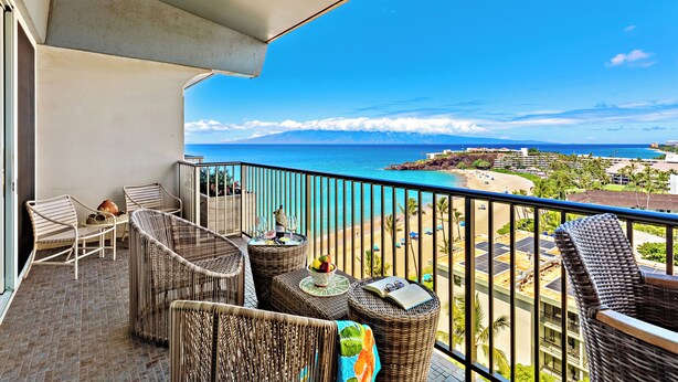 Ein Balkon mit Korbmöbeln, Blick auf den Strand und einen klaren Himmel.