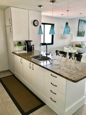 Enjoy meals in this kitchen with a central island, sink, and coffee maker, surrounded by a dining area and comfortable seating.