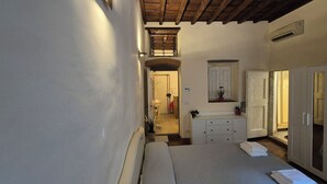 A narrow hallway leading to a bedroom with a bed, a dresser, and a mirror. There is a small window with a plant on the dresser. - Borgo San Frediano Hideaway  (Florence)