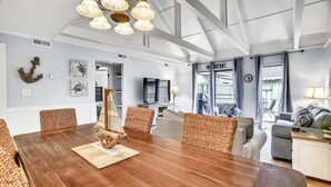 A spacious room with a wooden dining table, wicker chairs, a television, and a view of the outside. - Luxury Pet-Friendly Villa! Near Golf, Hilton Head (Hilton Head Island)