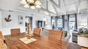 Una habitación amplia con una mesa de comedor de madera, sillas de mimbre, un televisor y vistas al exterior.