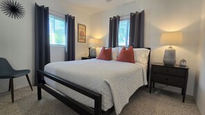 Une chambre à coucher avec un lit, deux tables de chevet, une chaise et une fenêtre avec des rideaux.