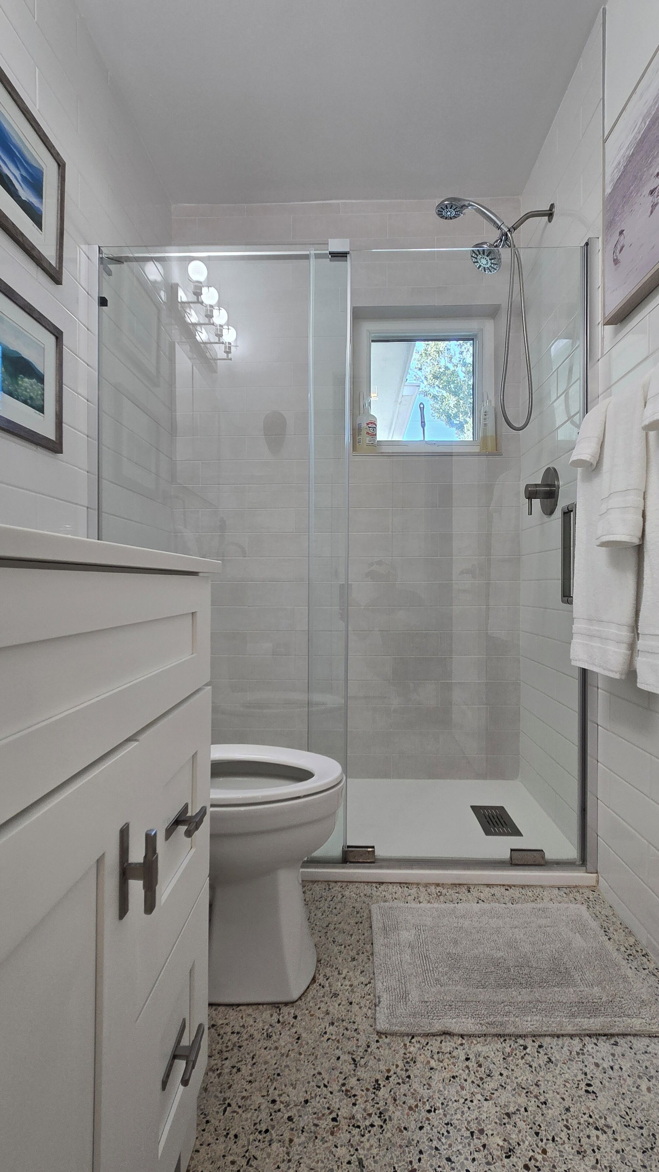 Een moderne badkamer met een glazen douchecabine, een toilet en een wastafel met lades.