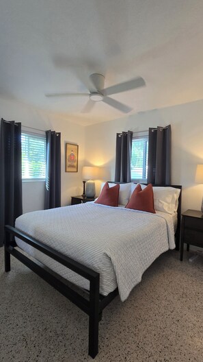 A bedroom with a bed, a ceiling fan, two bedside lamps, a nightstand, and a window with curtains.
