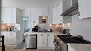 A modern kitchen with white cabinetry, a built-in dishwasher, a gas stove, and a coffee maker.