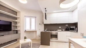A modern kitchen with white cabinets, a built-in oven, and a microwave. There is a small island with a sink and a white table with a plant. - Charming stay in Rome: Luxury apartment one step from St. Peter's Basilica (Roma)