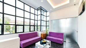 Eine moderne Lobby mit großen Fenstern, zwei violetten Sofas, einem weißen Couchtisch und einem Holzschrank.