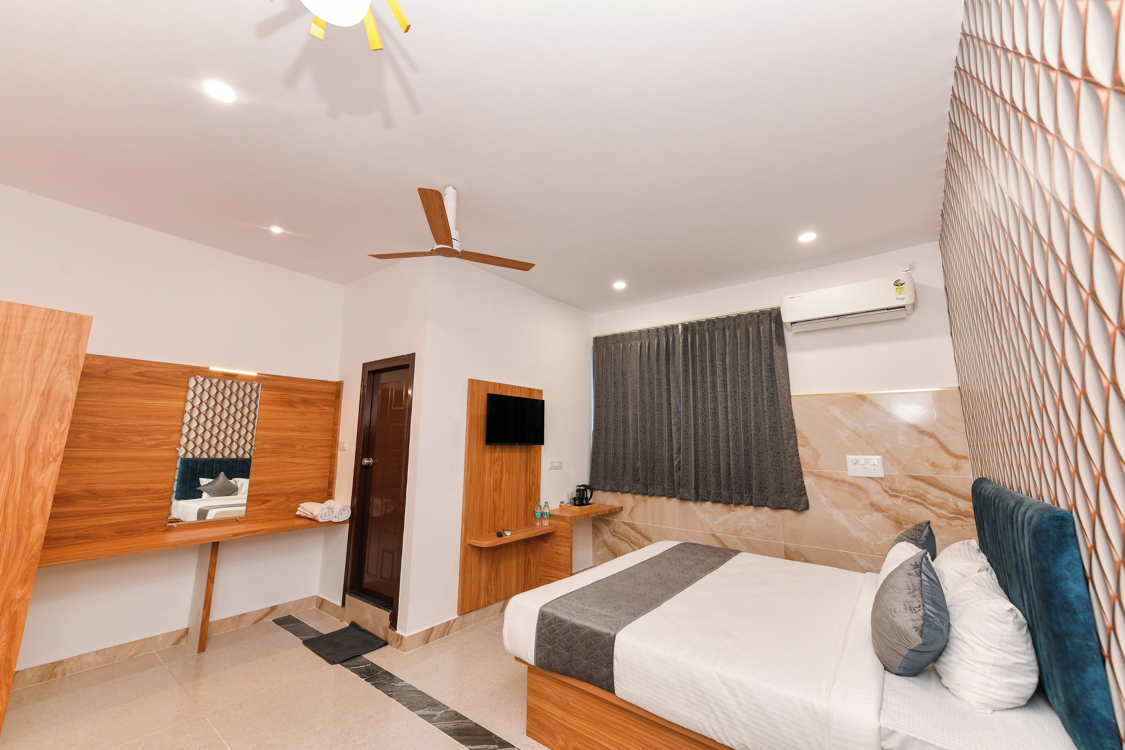 A hotel room with a bed, a desk, a ceiling fan, an air conditioning unit, and a TV.