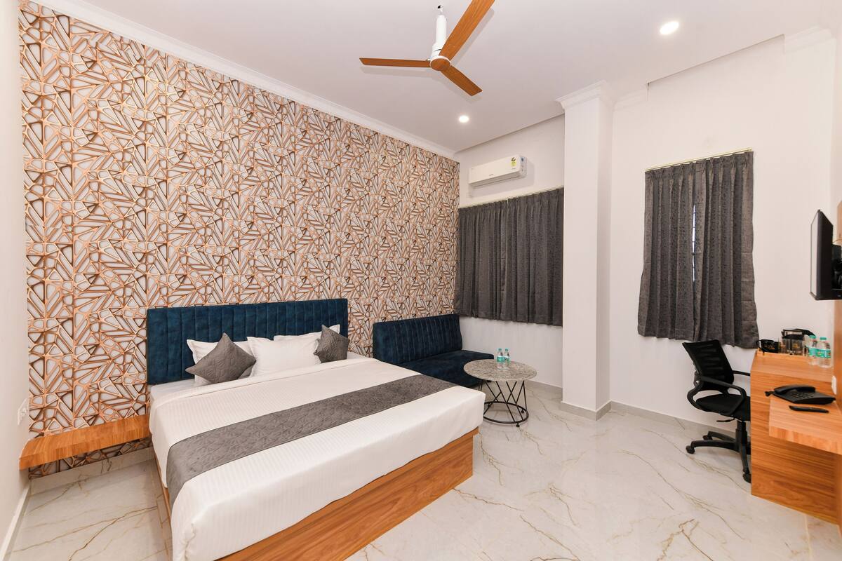 A modern bedroom with a geometric patterned wall, a large bed with a blue headboard, a desk with a computer, and a ceiling fan.