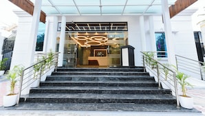 Ein Hotel mit gläserner Fassade, einer Rezeption und einer Treppe mit Metallgeländern.
