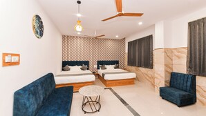 Ein modernes Hotelzimmer mit zwei Betten, einem blauen Sofa, einem runden Couchtisch und einem Deckenventilator.