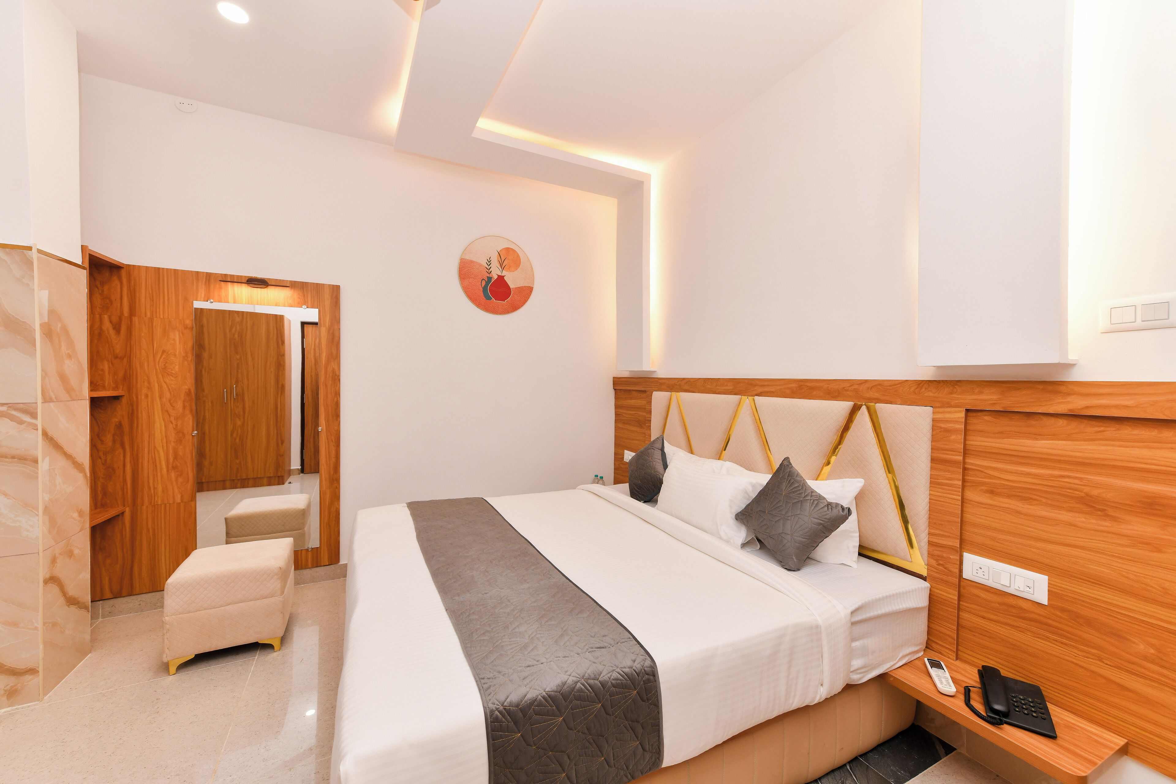 A modern hotel room with a large bed, wooden headboard, bedside table with a phone, and a small seating area.
