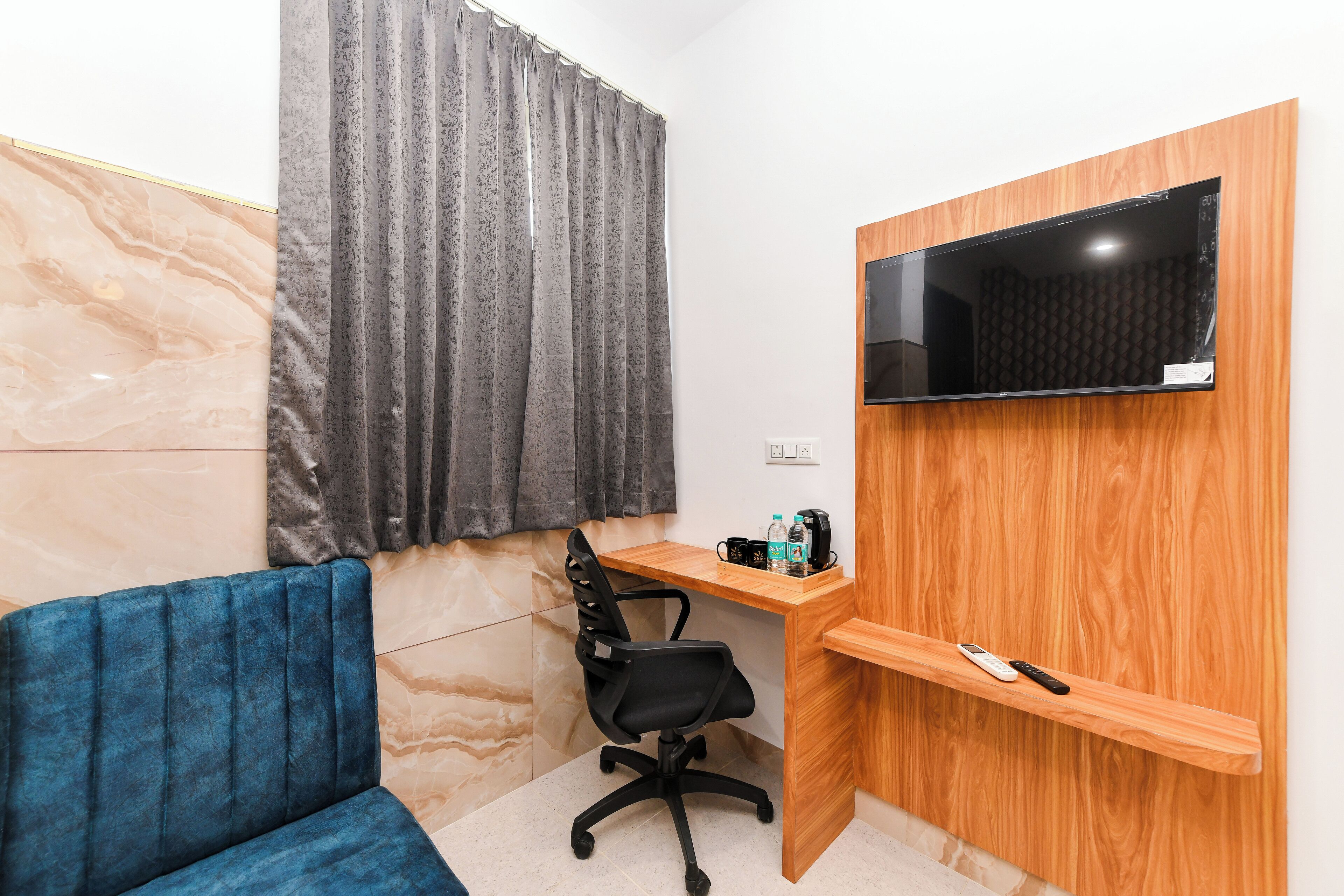 Una habitación pequeña y moderna con un sofá azul, un escritorio de madera con un televisor y una silla.