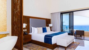 Habitació d'hotel moderna amb un llit gran, vista a l'oceà i un balcó amb una cadira.