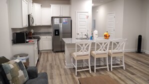 Una cocina moderna con armarios blancos, un refrigerador de acero inoxidable y un comedor con sillas y una mesa blancos.