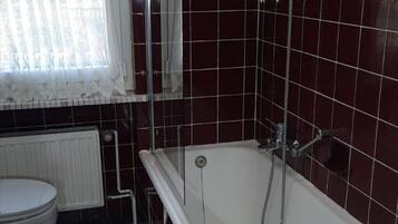 Une salle de bain avec une baignoire, des toilettes et une fenêtre avec un rideau.