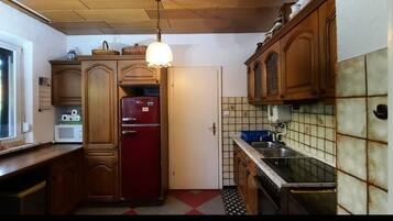 Une cuisine avec des meubles en bois, un réfrigérateur rouge, une fenêtre et un pare-feu en carrelage.