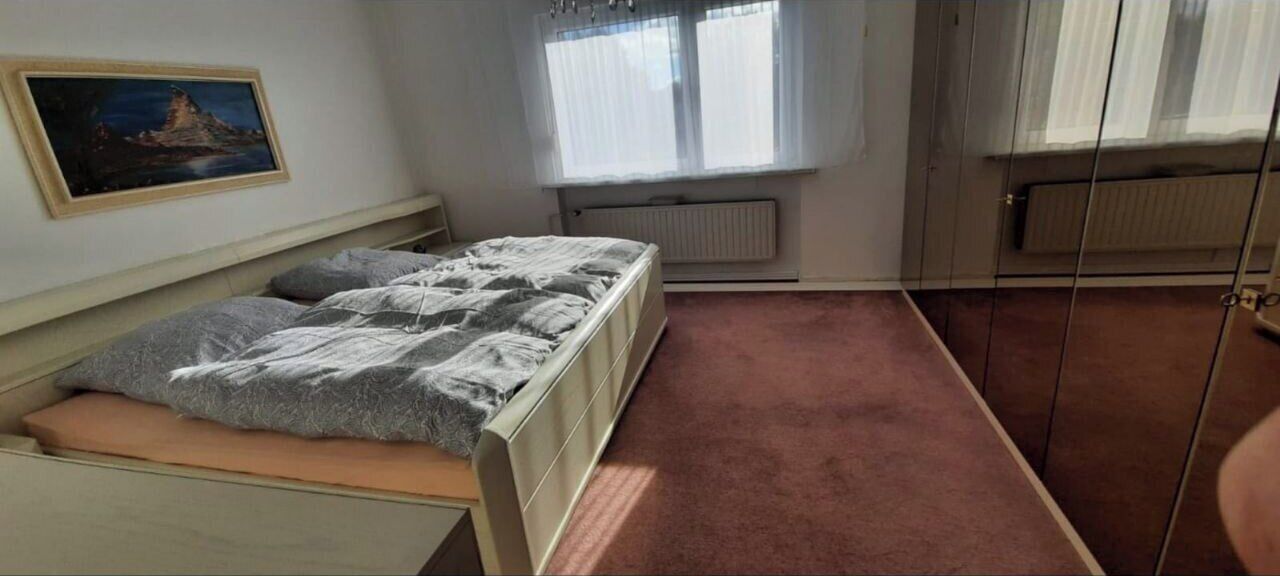 Une chambre à coucher avec un lit, un radiateur, une fenêtre avec des rideaux et un tableau accroché au mur.