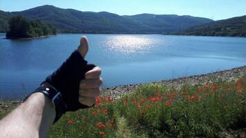 Eine Hand zeigt Daumen hoch, im Hintergrund ein See und Berge.