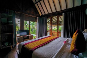 Relax in a spacious room with a large bed, TV, and views of lush greenery.