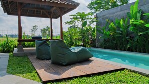 Una terrazza in legno con due poltrone sacco verdi, una piscina e vegetazione lussureggiante.