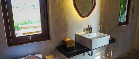 A bathroom with a toilet, a white sink, a mirror, and a window.