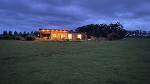 Una casa moderna con un ampio portico e una zona esterna coperta, immersa in un prato e alberi.