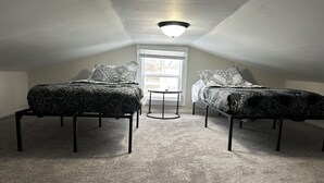 Une petite chambre mansardée avec deux lits, une petite table et une fenêtre.