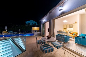 Une terrasse extérieure moderne, dotée d’une balustrade en verre, d’une piscine et d’un coin repas avec des chaises à rayures bleues et une table ronde.