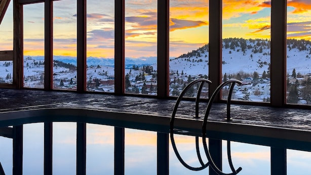 Área da piscina com vista para uma paisagem nevada e montanhas ao pôr do sol.