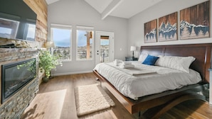 Quarto com lareira de pedra, uma cama grande, vista pela janela e teto de madeira.