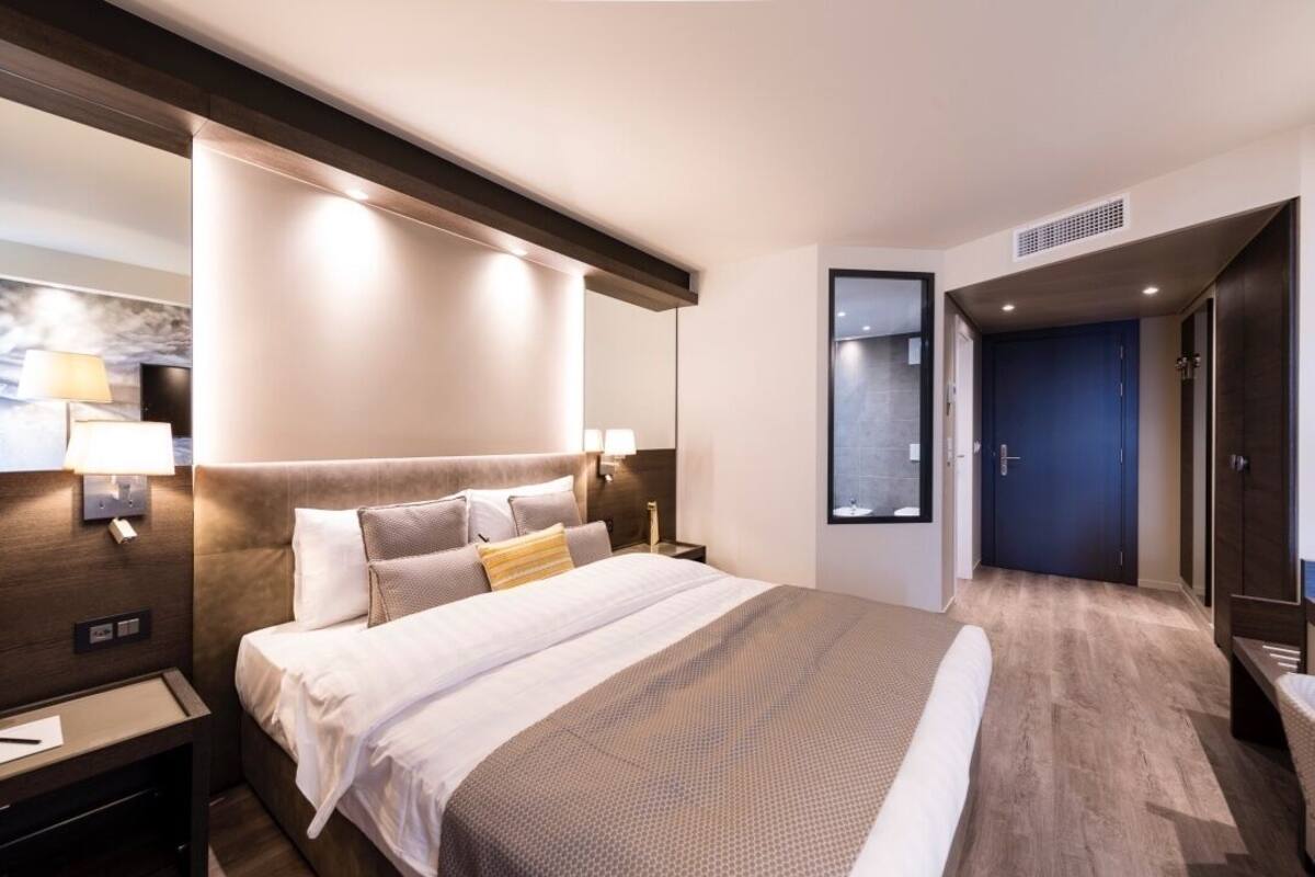 A modern hotel room with a large bed, bedside lamps, a nightstand, and a wardrobe.