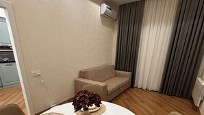 Un coin repas avec une table ronde dressée pour quatre personnes, un canapé beige et un climatiseur fixé au mur.